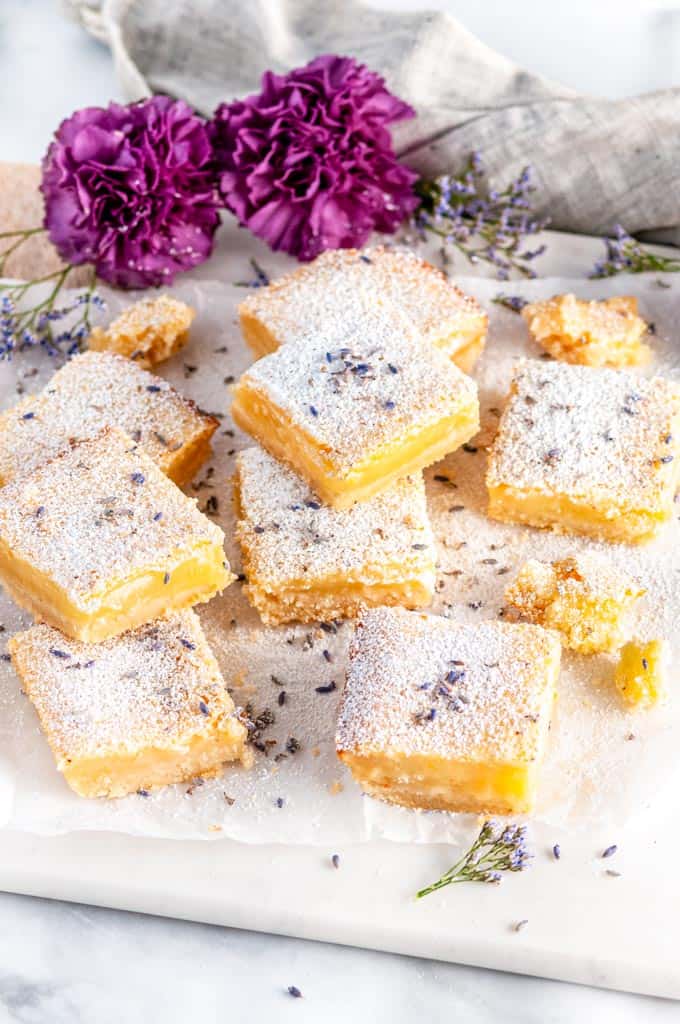 Lavender Lemon bars with powdered sugar and purple flowers on parchment