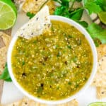 Roasted Tomatillo Salsa Verde in food processor with chips, limes, and cilantro in white bowl on white marble overhead