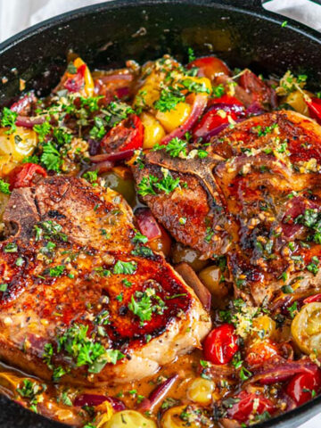 Skillet Balsamic Pork Chops with Tomatoes and Gremolata in black cast iron lodge skillet on white marble