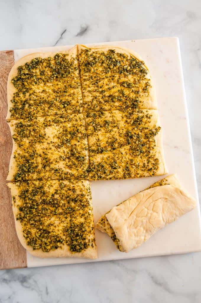 Pull Apart Pesto Bread dough unbaked on wood and marble board over head sliced into squares with one roll