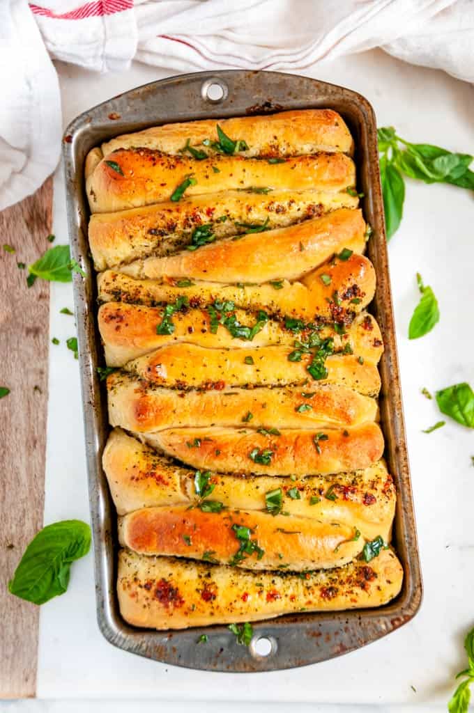 Pull Apart Pesto Bread in loaf pan with basil on wood and white marble board over head