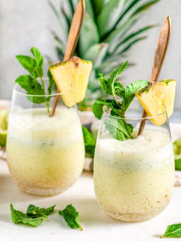 Skinny Piña Colada Cocktail in gold speckled stemless wine glasses with gold spoons and fresh mint on white marble side view