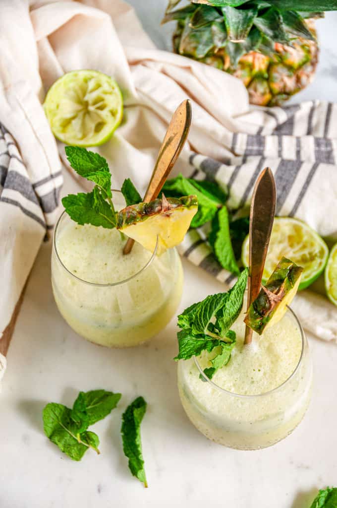 Skinny Piña Colada Cocktail in gold speckled stemless wine glasses with gold spoons and fresh mint on white marble over head