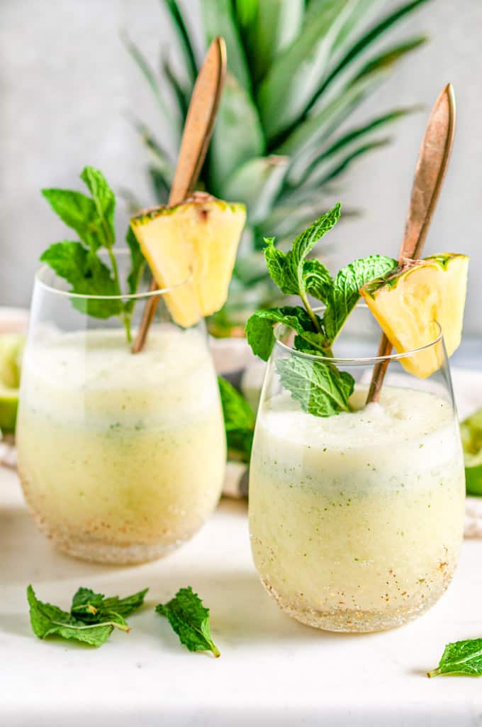 Skinny Piña Colada Cocktail in gold speckled stemless wine glasses with gold spoons and fresh mint on white marble side view