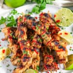 Grilled Lime Chicken Skewers with lime slices, cilantro, and a Sriracha drizzle on a gray plate angled over head view