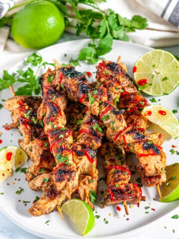 Grilled Lime Chicken Skewers with lime slices, cilantro, and a Sriracha drizzle on a gray plate angled over head view