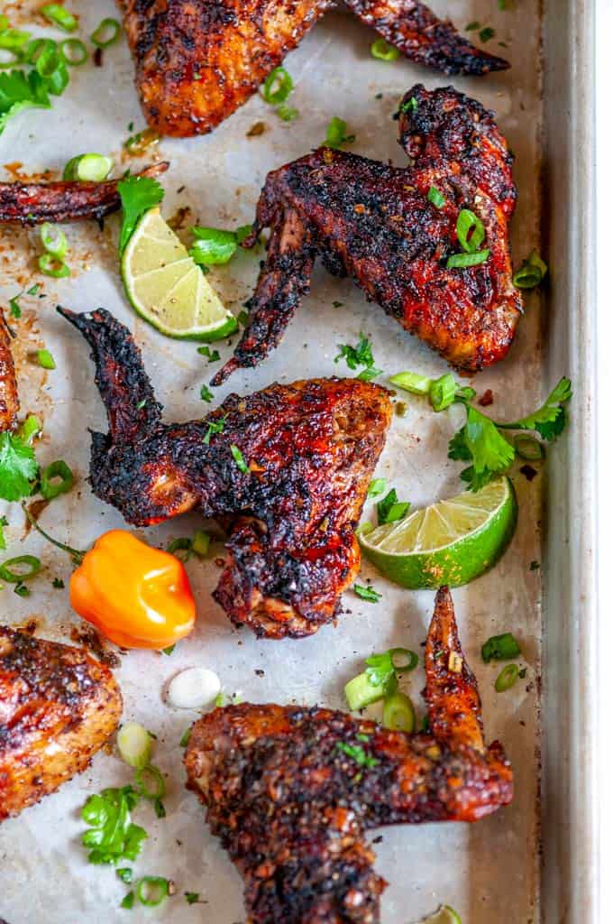 Jamaican Jerk Chicken Wings (Air Fryer + Oven Baked Methods) on sheet pan with limes and habanero pepper close up