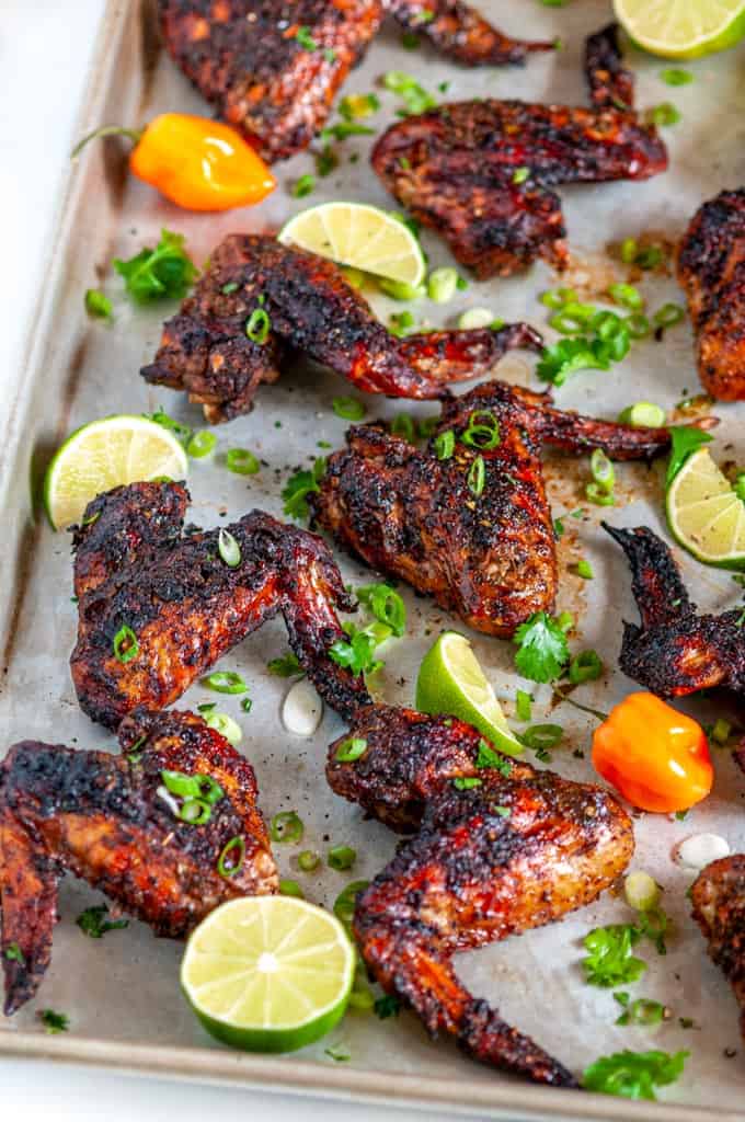 Jamaican Jerk Chicken Wings (Air Fryer + Oven Baked Methods) on sheet pan with limes and habanero pepper side view
