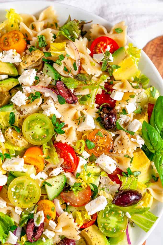 Summertime Greek Pasta Salad in white bowl with wood spoon overhead view close up