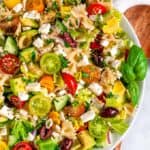 Summertime Greek Pasta Salad in white bowl with wood spoon overhead view close up