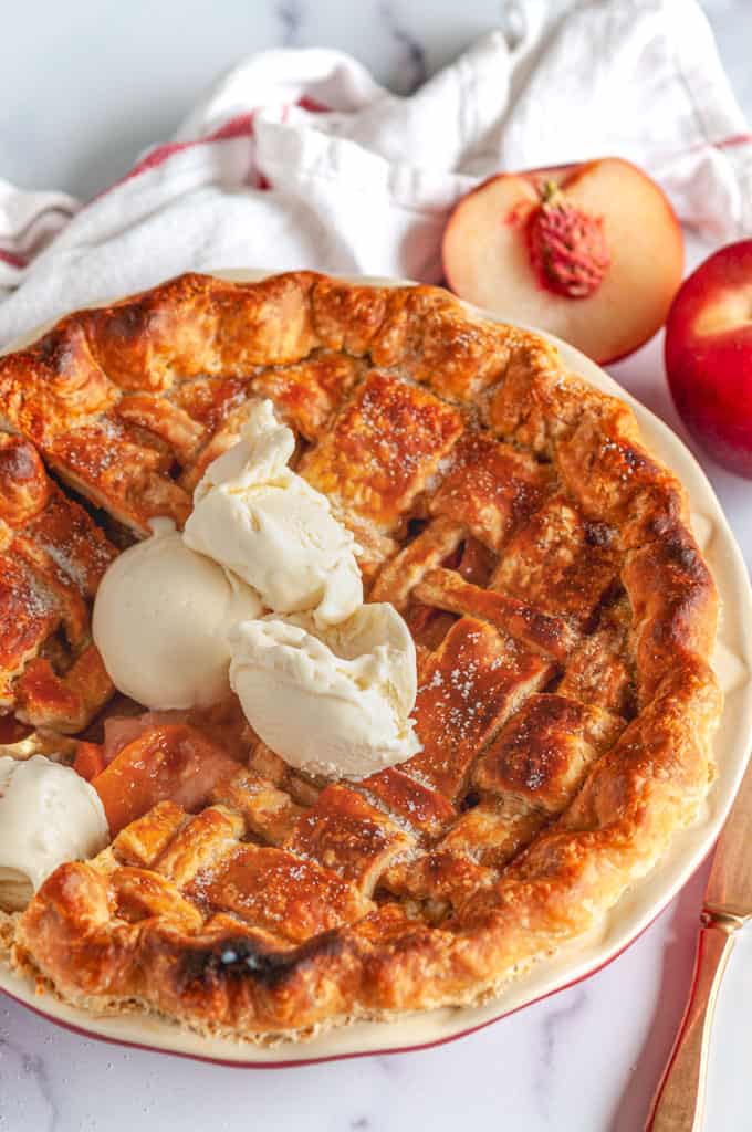 Summer Peach Pie in red pie pan on white marble with French vanilla ice cream over head view