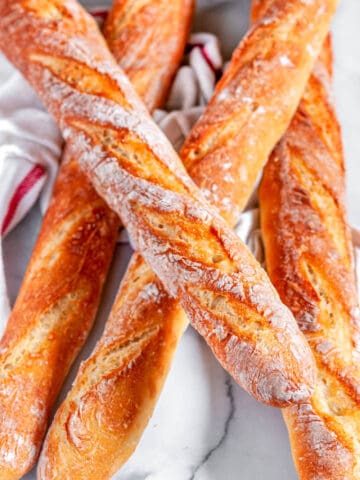 Classic crusty French baguettes with tea towel on white marble over head view