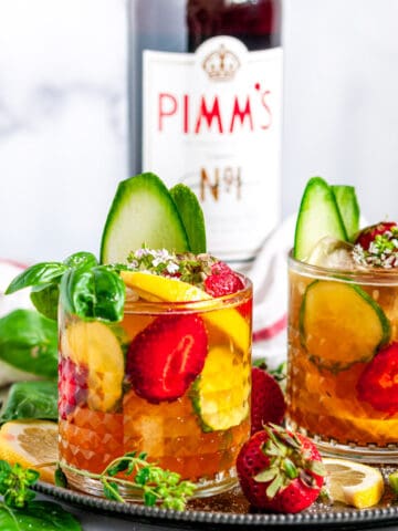 Classic Pimm's Cup Cocktail with lemon, cucumber, and strawberry slices garnished with basil leaves in glasses side view