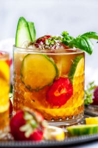 Classic Pimm's Cup Cocktail with lemon, cucumber, and strawberry slices garnished with basil leaves in glass side view close up