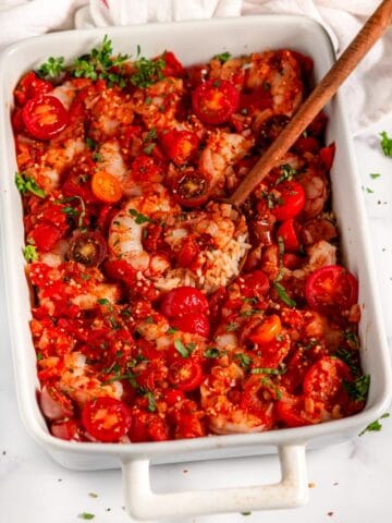 Healthy Italian Shrimp and Rice Casserole in white dish with tea towel and wooden spoon