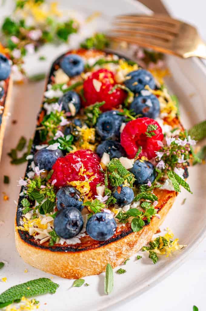 Lemon Berry Breakfast Toast with fresh herbs on gray plate with tea towel and gold utensils side view close up