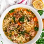 Italian Wedding Soup in white bowl with gold spoon, spinach, and a squeezed lemon
