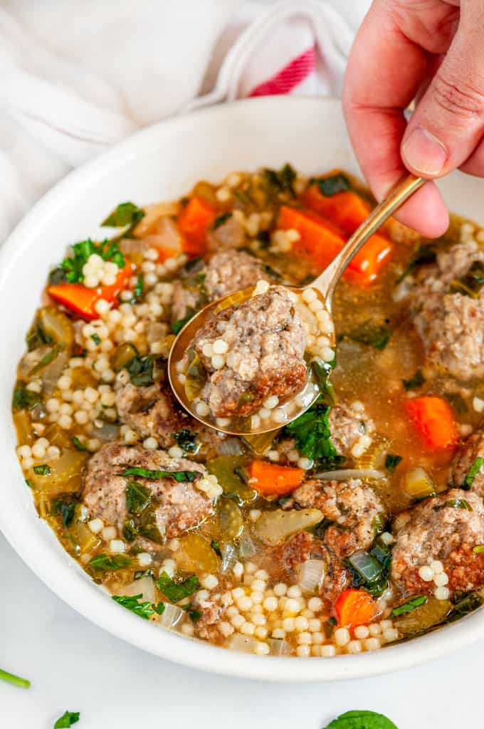 Italian Wedding Soup in white bowl with spoonful held above by hand