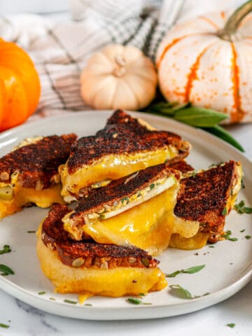 Pumpkin Grilled Cheese Sandwich on gray plate with apple slice and sage on white marble