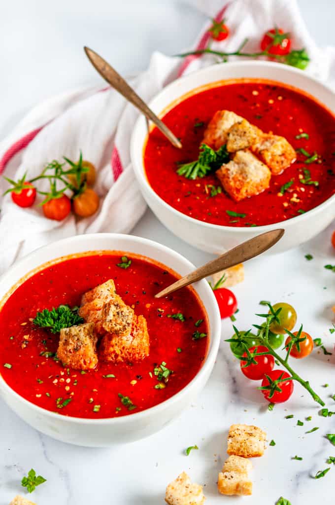 Roasted Bell Pepper Tomato Soup with croutons, parsley and gold spoons in white bowls
