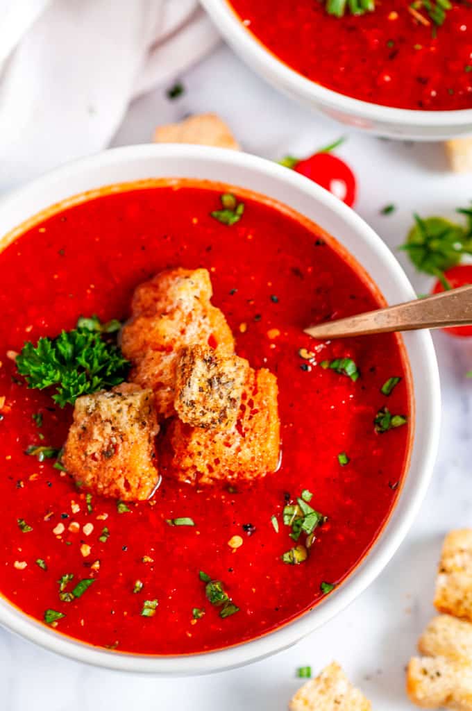 Roasted Bell Pepper Tomato Soup with croutons, parsley and gold spoon in white bowl