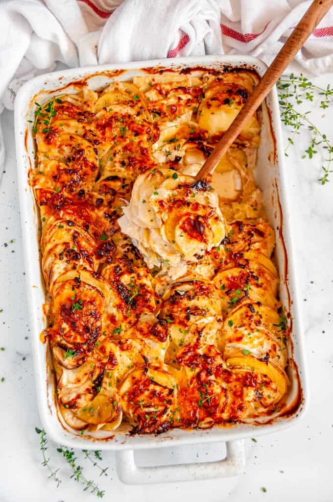 Root Vegetable Gratin in white casserole dish on white marble with wood spoon and tea towel
