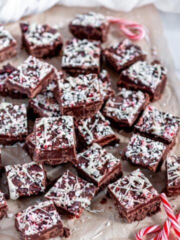Holiday Chocolate Peppermint Fudge with holiday sprinkles and crushed candy canes on parchment