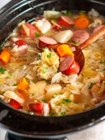 Slow Cooker Kielbasa Cabbage Stew in crock pot with wooden spoon