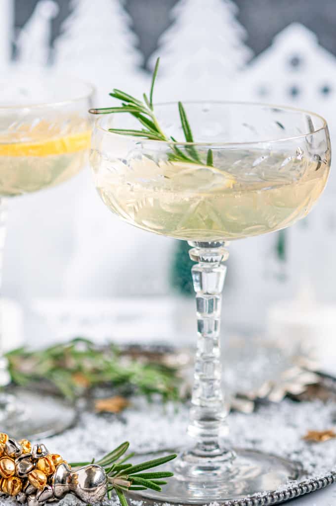 Sparkling Elderflower Gin Cocktail in crystal glasses with rosemary, lemon slices, and paper holiday village in background