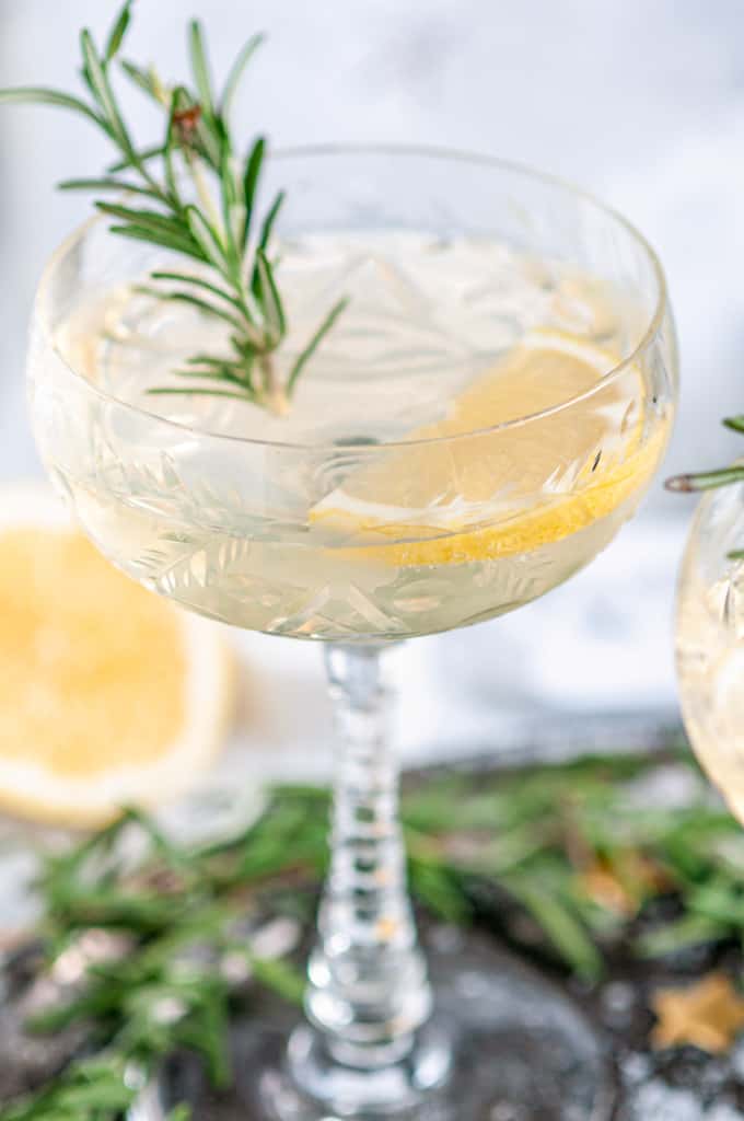Sparkling Elderflower Gin Cocktail in crystal glass with rosemary, lemon slices, and paper holiday village in background