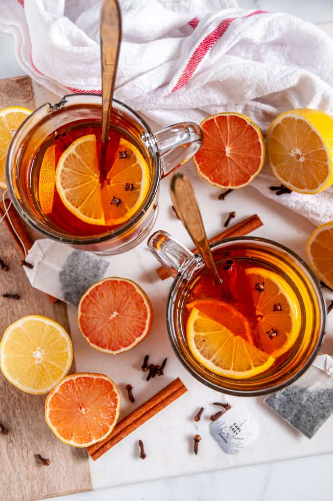 Cozy Winter Earl Grey Hot Toddy in glass mugs with lemon slices, cloves, and gold spoons on white marble