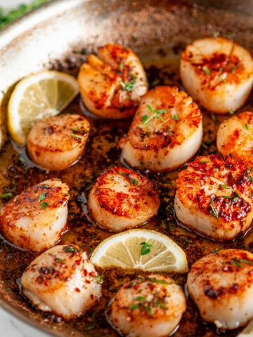 Pan Seared Lemon Garlic Butter Scallops in all-clad skillet with lemon slices on white marble