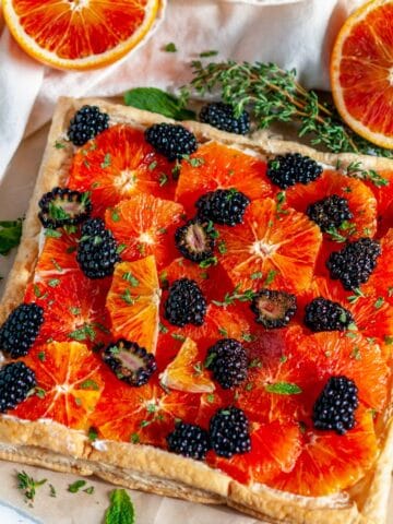 Blood Orange Blackberry Mascarpone Tart on brown parchment with fresh thyme and mint leaves