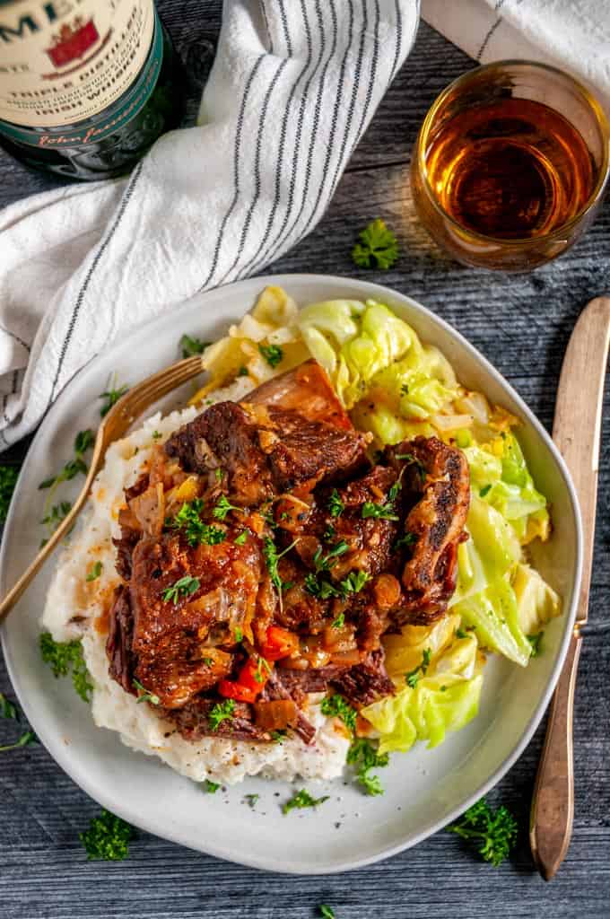 Instant Pot Whiskey Braised Short Ribs on gray plate with Jameson in a glass, mashed potatoes and cabbage