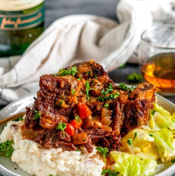 Instant Pot Whiskey Braised Short Ribs on gray plate with Jameson in a glass, mashed potatoes and cabbage