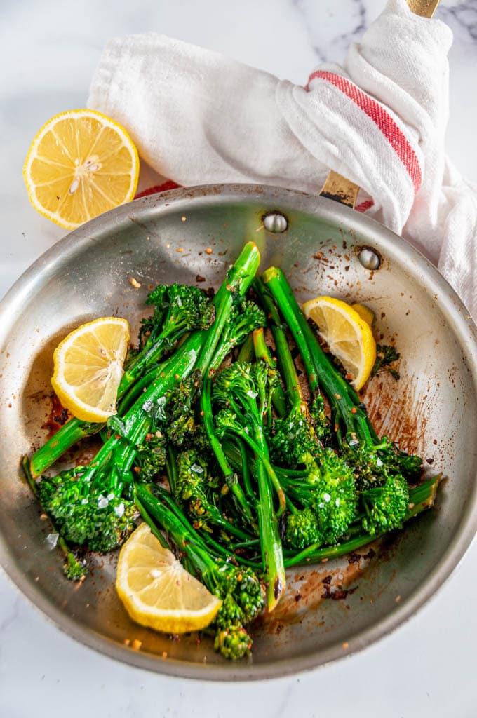 Quick and Easy Lemon Garlic Broccolini in skillet with lemon wedges and tea towel