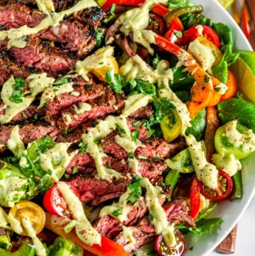 Steak Fajita Salad with Cilantro Avocado Dressing in white bowl on marble with lime slices and copper serving ware