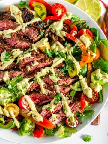 Steak Fajita Salad with Cilantro Avocado Dressing in white bowl on marble with lime slices and copper serving ware
