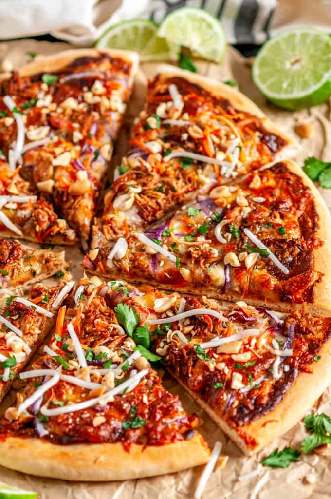 Thai Chicken Pizza on brown parchment paper cut into slices with lime slices