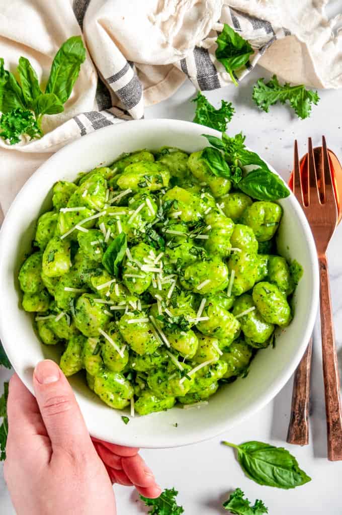 Creamy Kale Pesto Gnocchi in white bowl held by hand with copper fork and spoon