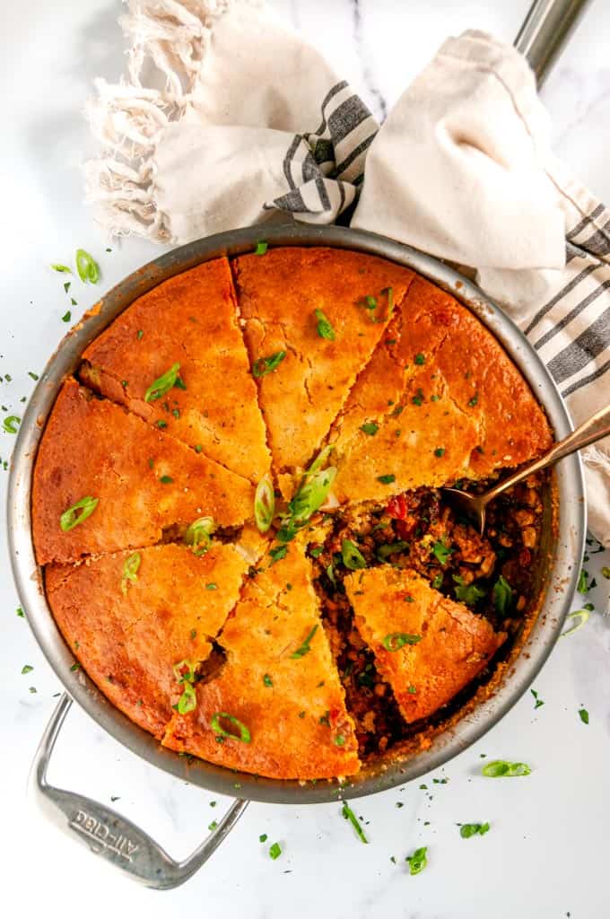 Homemade Cornbread Tamale Pie in All-Clad skillet with gold spoon on white marble