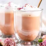 Rose Bud Earl Grey Tea Latte in glass mugs with gold spoons and pink flowers on gray plate