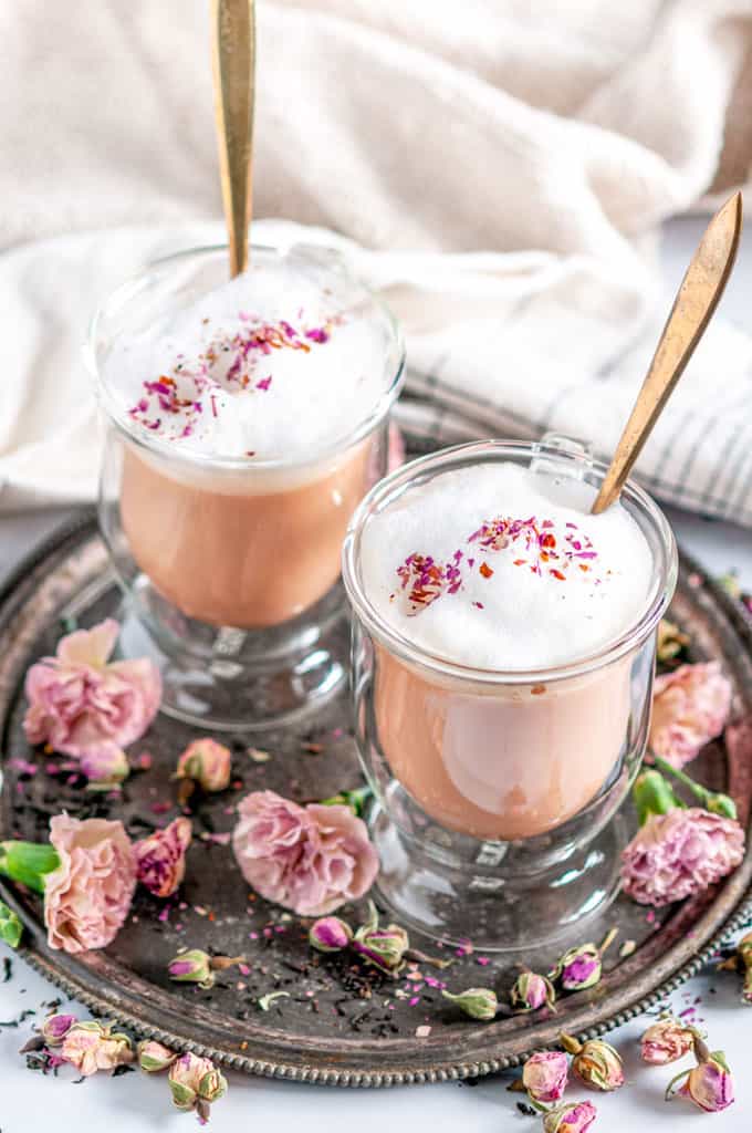 Rose Bud Earl Grey Tea Latte in glass mugs with gold spoons and pink flowers on gray plate