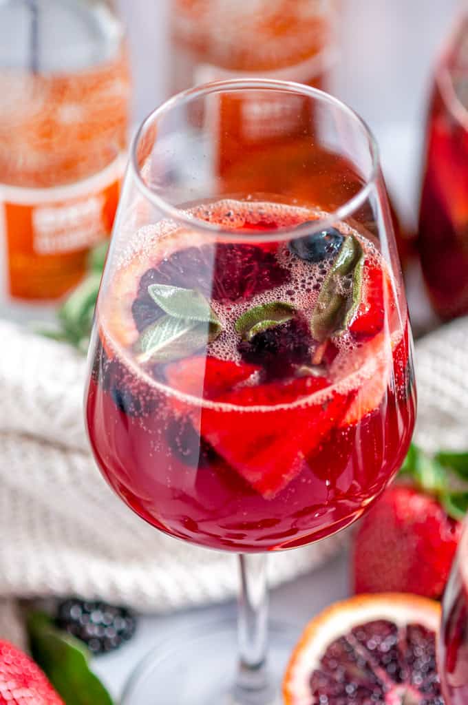 Sparkling Rosé Blood Orange Sangria with fresh sage leaves in glass on white marble close up