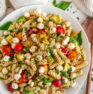 Caprese Pesto Pasta Salad in white bowl with wood spoon on marble