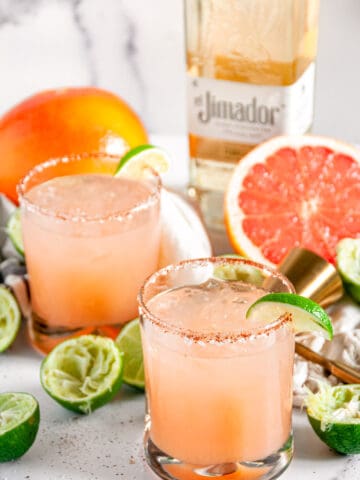 Classic Fresh Grapefruit Paloma in chili salt rimmed glasses and El Jimador tequila bottle in the background on white marble