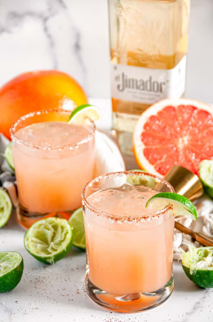 Classic Fresh Grapefruit Paloma in chili salt rimmed glasses and El Jimador tequila bottle in the background on white marble