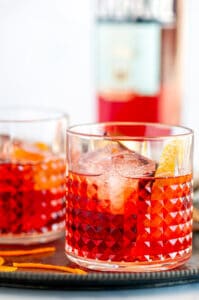 Classic Negroni Cocktail in two glass with ice, orange peels and Campari bottle in background