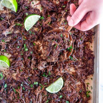 Instant Pot Barbacoa Beef on sheet pan and parchment paper spoonful held in hand with lime slices