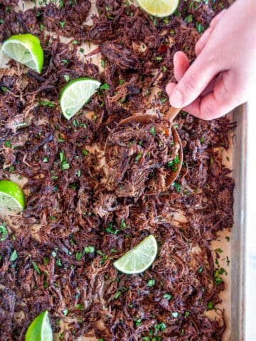 Instant Pot Barbacoa Beef on sheet pan and parchment paper spoonful held in hand with lime slices